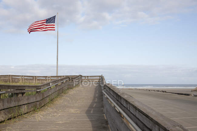 Boardwalk through grassland with mountains and American flag flying. — Stock Photo