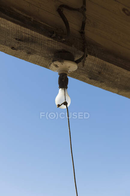 Old incandescent light bulb on a porch beam with a string pull control — Fotografia de Stock