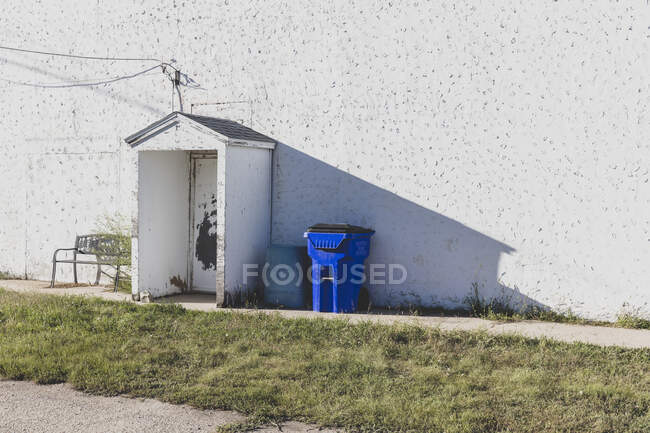 Біла стіна будинку в маленькому містечку, блакитний смітник і лавка.. — стокове фото