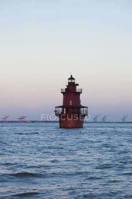 Un faro en la bahía de Chesapeake, vista de la costa con grandes grúas elevadoras de los puertos. - foto de stock