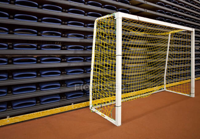 Pilha de assentos dobrados em um local de esportes indoor e uma rede de gol de futebol prática. — Fotografia de Stock