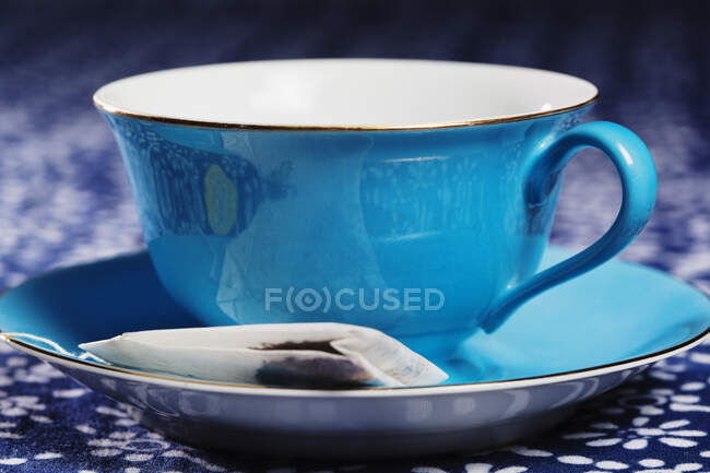 A cup and saucer, blue colour, a tea bag in the saucer. — Stock Photo