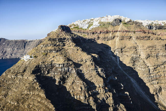 As falésias e formações rochosas de uma ilha no mar Egeu, com uma cidade de casas brancas no topo das falésias. — Fotografia de Stock
