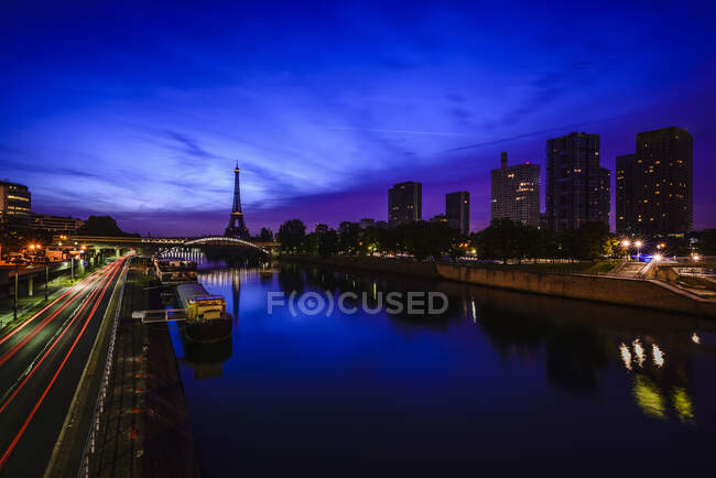 Uma vista ao longo da água do Rio Sena à noite, edifícios altos na margem do rio, a torre Eiffel à distância. — Fotografia de Stock