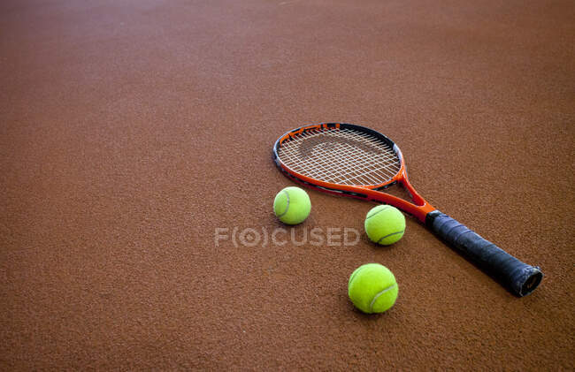 Una pista de tenis dura y un raquet de tenis, con tres bolas. - foto de stock
