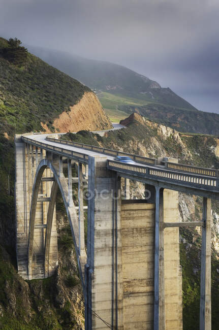 A car on a bridge on the Big Sur Pacific coastline, mountains and mist. — Stock Photo