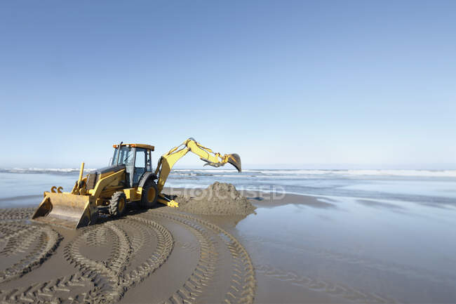 A backhoe, digger with large scoop working on the soft sand at the water's edge. — Stock Photo