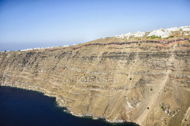 Los acantilados y formaciones rocosas de una isla en el mar Egeo, con una ciudad de casas blancas en la parte superior de los acantilados. - foto de stock