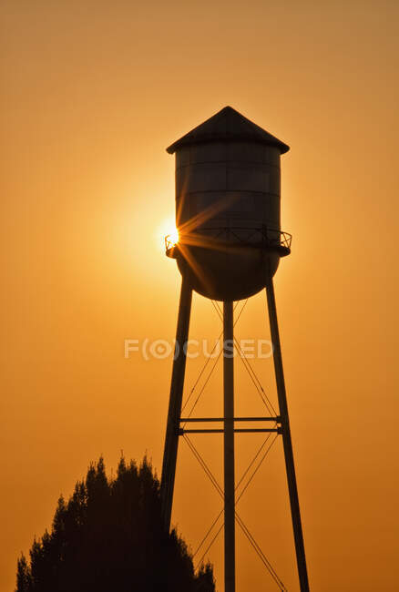 Sole che tramonta dietro la torre dell'acqua agricola. — Foto stock