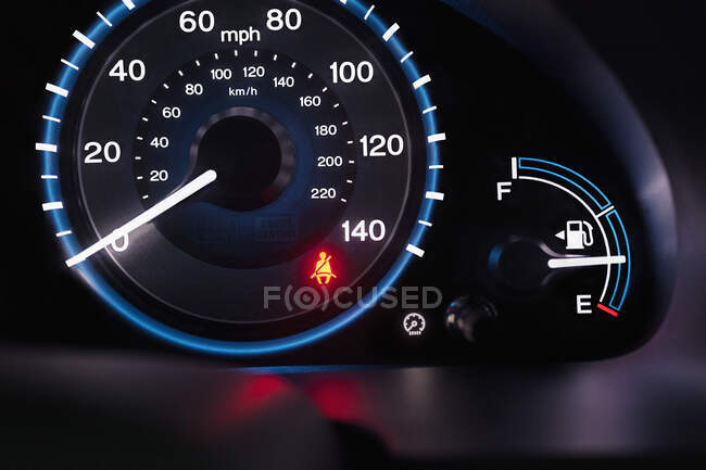 A lit up car dashboard, mph speed dial, in miles and kilometres, fuel guard and a red warning seatbelt light. — Stock Photo