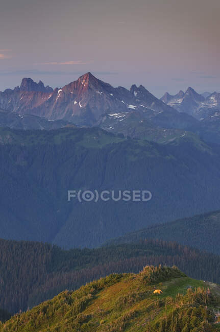 Vista de cima, uma pequena tenda laranja montada em um cume, com vista para o vale e serra além. — Fotografia de Stock