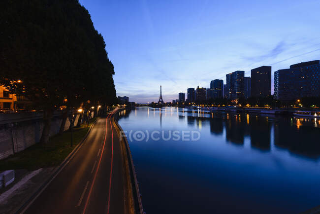 Vista a lo largo del río Sena hasta la torre Eiffel, el terraplén del río y la ciudad al atardecer, reflejos sobre el agua. - foto de stock