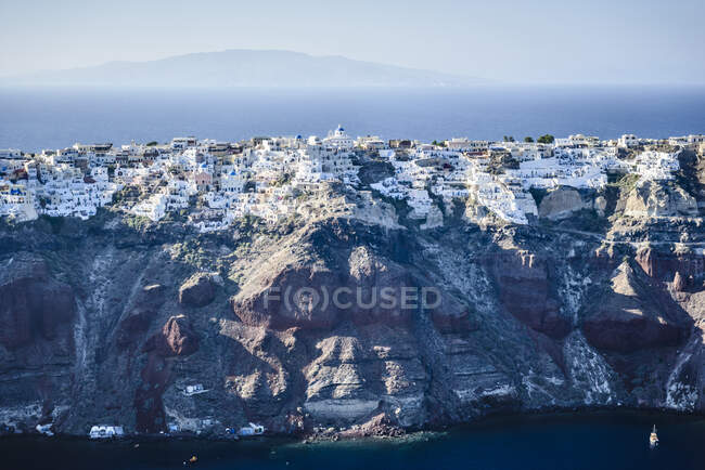 Vista aérea de uma ilha nos mares azuis profundos do mar Egeu, formações rochosas, casas caiadas de branco empoleiradas nas falésias. — Fotografia de Stock