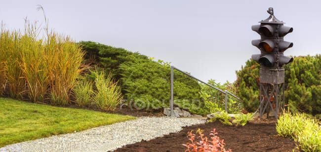 Traffic light in a garden, flower border with shrubs and path. — Stock Photo