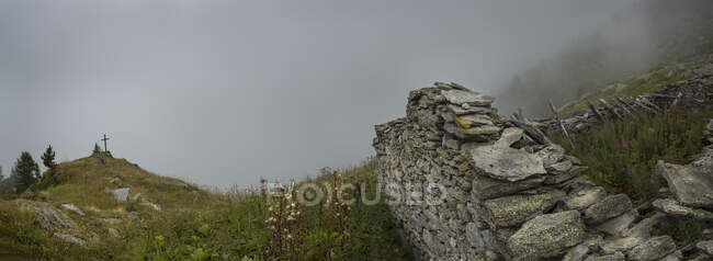 Um santuário de montanha pelo caminho na região alpina perto de Mont Blanc, uma cruz perto de Fenetre D 'Arpette, nuvens baixas e névoa. — Fotografia de Stock