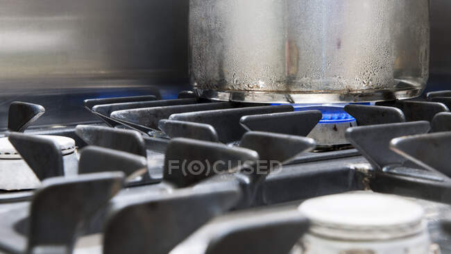 Close-up de uma panela de metal em uma placa de gás, chamas azuis aquecendo a panela. — Fotografia de Stock