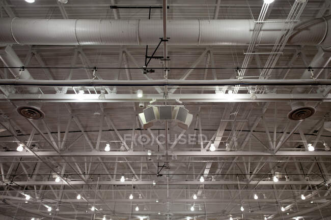 Le plafond d'un grand bâtiment, avec des conduits d'air et des tuyaux, les chevrons, portiques et entretoises, haut-parleurs de système de son, lumières et unités d'extraction. — Photo de stock