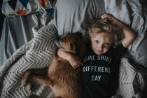 Хлопчик лежить у ліжку зі своїм собакою — стокове фото