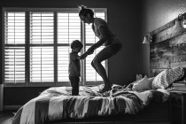 Madre con su hijo saltando juntos en la cama - foto de stock