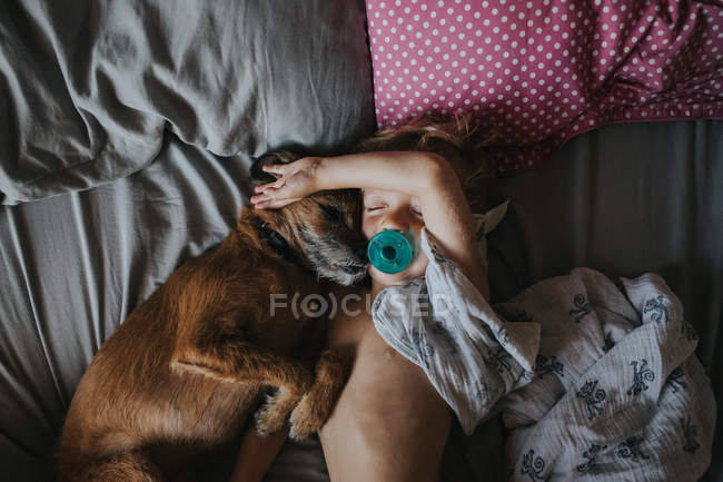 Boy cuddling in bed with his dog — Stock Photo