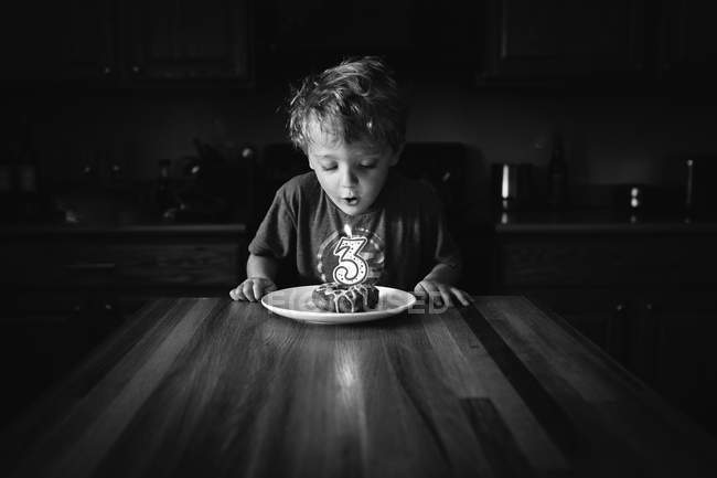 Boy blowing out a candle in birthday donut — Stock Photo