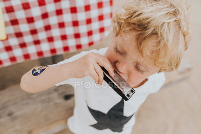 Blond garçon jouer un harmonica — Photo de stock