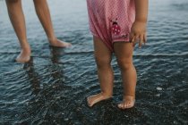 Pernas de menina em pé na água na praia de areia — Fotografia de Stock