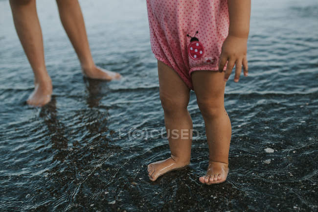 Дівчина стоїть на воді на піщаному пляжі — стокове фото