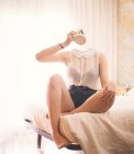 Headless woman siiting on bed and drinks — Stock Photo