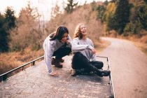 Smiling young women on car roof — Stock Photo