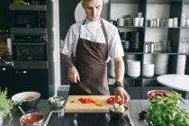 Man in apron cutting vegetables — Stock Photo