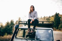 Jeune femme assise sur le toit de la voiture — Photo de stock