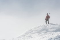 Escalador en la cima de la montaña nevada - foto de stock