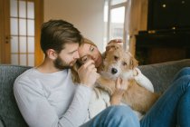 Coppia accarezzando cane su divano — Foto stock