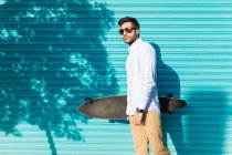 Молодий чоловік в сонцезахисних окулярах тримає скейтборд — стокове фото