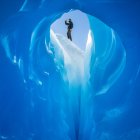 Shot from inside of glacier cave of man standing outside in bright sunlight. — Stock Photo
