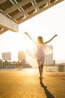 Portrait of young ballet dancer performing ballet with flying skirt and arms up against sunrise. — Stock Photo