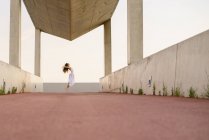 Visão de nível de superfície para jovem morena em vestido branco realizando balé em construção — Fotografia de Stock