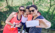 Retrato de madres felices y sus hijos tomando selfie vía teléfono móvil en el parque - foto de stock