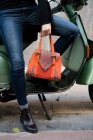 Une femme méconnaissable tenant un sac à main orange assis sur le scooter. — Photo de stock