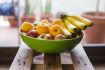 Fresh fruits in bowl on wooden surface — Stock Photo
