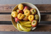 Fresh fruits in bowl on wooden surface — Stock Photo