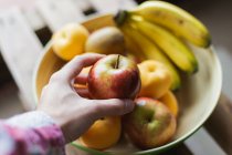 Крупним планом людська рука бере яблуко з миски зі свіжих фруктів — стокове фото