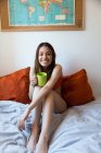 Fröhliches Mädchen mit Tasse auf dem Bett — Stockfoto