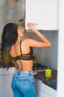 Female standing in kitchen opening cupboard — Stock Photo