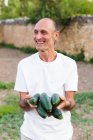 Lächelnder Bauer mit Zucchini-Kürbissen in der Hand und Blick zur Seite — Stockfoto