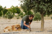 Man digging hole in ground beside tree by  golden retriever — Stock Photo