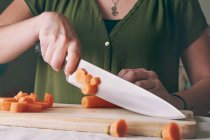 Primo piano della donna che taglia la carota fresca sul tagliere di legno — Foto stock