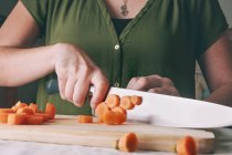 Close-up de mulher cortando cenoura fresca em tábua de corte de madeira — Fotografia de Stock