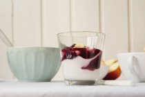 Боковой вид на стакан йогурта с джемом за кухонным столом — стоковое фото